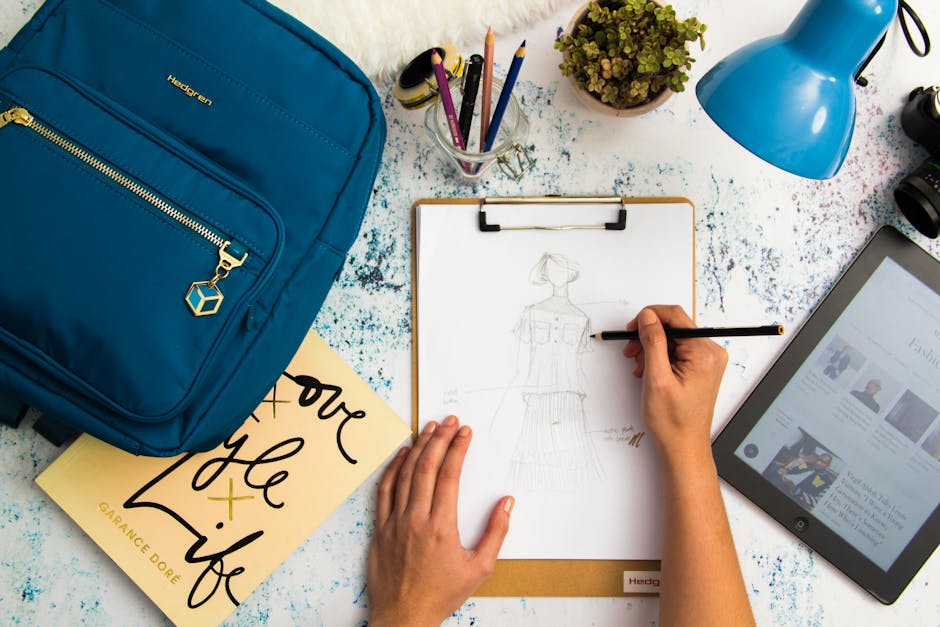 Top view of a designer sketching fashion ideas in a creative workspace with various tools.